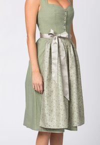 Grünes Kleid mit weißen Punkten, quadratischem Ausschnitt, Knopfleiste und satiniertem Schleifen-Gürtel. Der Rock hat ein florales Muster in hellgrünen Tönen.