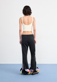 Black athletic pants with side stripes, featuring colorful, wavy fabric accents at the hem, paired with a white ribbed crop top.