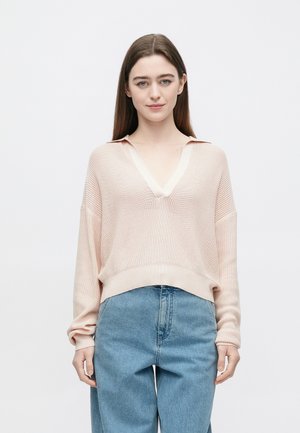 Hellrosa übergroßer Pullover mit V-Ausschnitt und Kragen, mit geripptem Strukturmuster und langen Ärmeln, kombiniert mit hoch taillierter blauer Jeans.