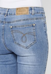 Faded blue denim jeans featuring a brown leather tag, signature stitching design on the back pocket, and metal rivet accents.
