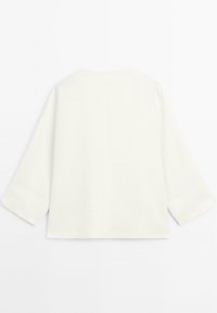Haut en lin blanc avec une coupe ample, un col rond et des manches trois-quarts. Texture lisse et design minimaliste sans embellissements.