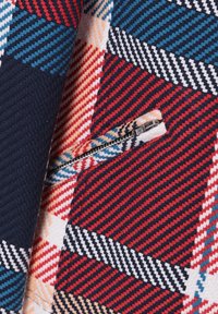 Tissu à carreaux coloré avec des rayures rouges, bleu marine, blanches et bleues, doté d'une fermeture éclair argentée partiellement ouverte.