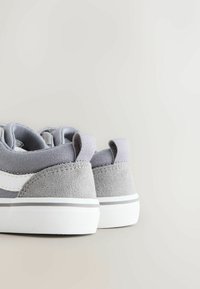 Par grå og hvide afslappede sneakers med ruskindsdetaljer og trækflapper, vist bagfra på en lys baggrund.