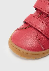 Κόκκινο δερμάτινο παπούτσι με υφή, διαθέτει δύο ρυθμιζόμενους ιμάντες με βέλκρο και καουτσούκ σόλα. Στρογγυλεμένη μύτη και διακριτικές ραφές.