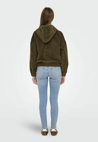 Olivgrön kordfläskhuva med dragsko i huvan, elastiska ärmslut och midja. Matchas med ljusblå smala jeans och bruna mönstrade skor.