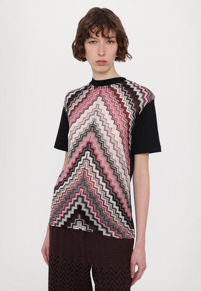 Camiseta de manga corta con un patrón de zigzag multicolor en rosa, negro y blanco, con la parte trasera completamente negra. Textura suave, ajuste casual.