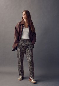 Braune Lederjacke, weißes Tanktop, graue Leopardenmuster-Hose und mehrfarbige Sneaker. Lockerer Schnitt mit Cargotaschen.