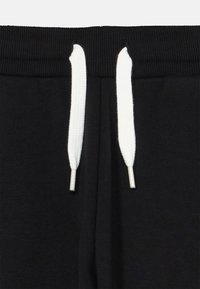 Svarta sweatpants har ett strukturerat midjeband med vita dragsnören, och visar en slät tyg utan mönster eller anmärkningsvärda detaljer.