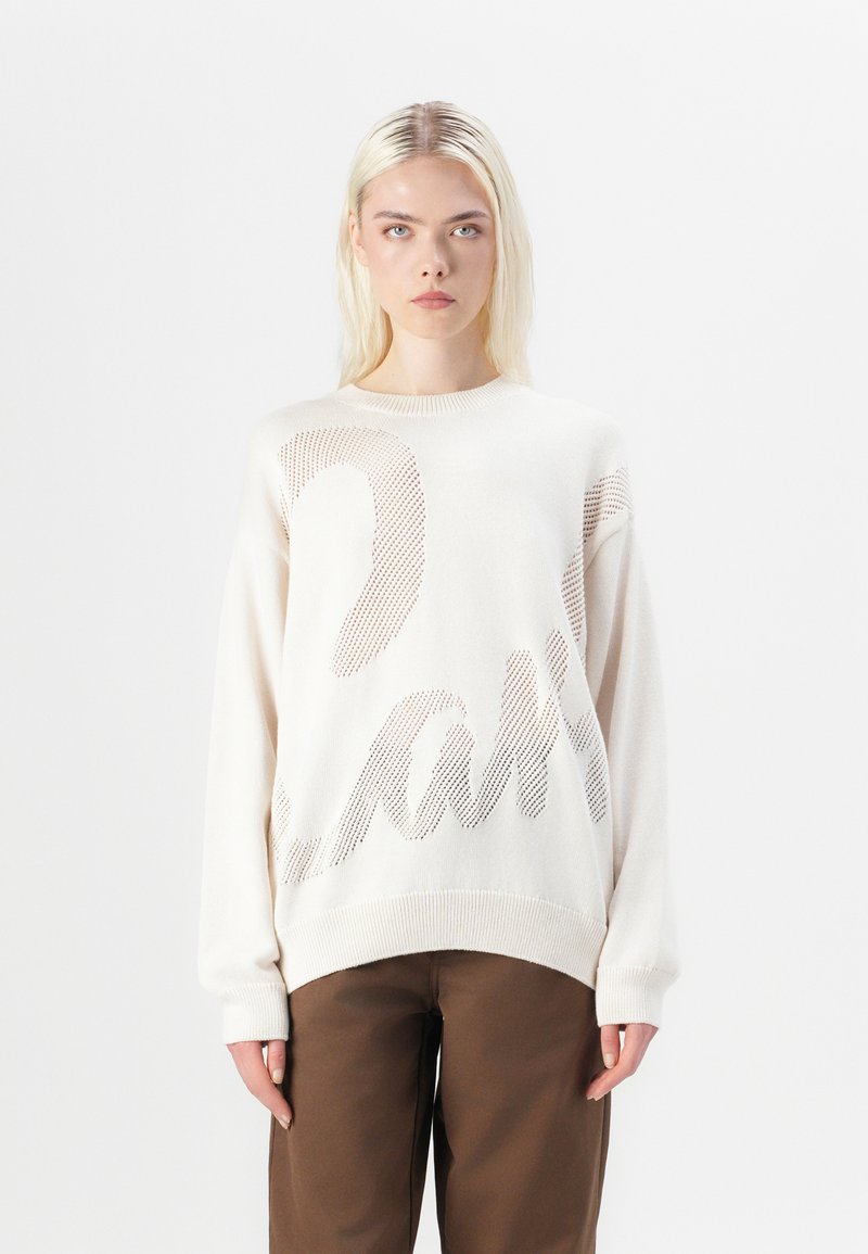 Krämfärgad stickad tröja med lös passform, med en texturerad, nätliknande design och ett djärvt grafiskt mönster i brunt över framsidan.