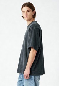 Perteklinis tamsiai pilkas medvilninis marškinėlis su trumpomis rankovėmis, apvalia iškirpte ir minkštu, nublukusiu tekstūru, derinamas su šviesiai mėlynomis džinsinėmis kelnėmis.