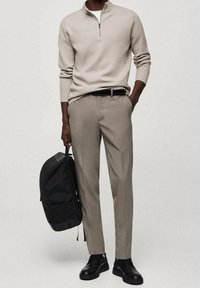 Helles beiges Zip-Hoodie, graue Hose, schwarzer Gürtel, schwarze Sneaker und ein schwarzer Rucksack. Glattes Material mit einem taillierten Design.