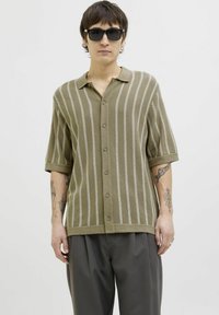 Kortærmet, olivengrøn strikket poloshirt med lodrette striber, knapfront og ribbet krave. Båret sammen med afslappede grå bukser.