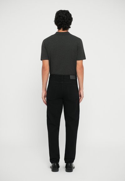 Pantaloni din denim negri cu buzunare la spate, asociați cu un tricou polo cu mânecă scurtă de culoare gri închis. Materialul este neted, cu un design simplu și fără logo-uri vizibile.