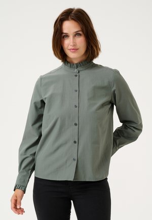 Button-up shirt in sage green, made of smooth fabric. Features a ruffled collar and long sleeves with gathered cuffs. Dark button accents.