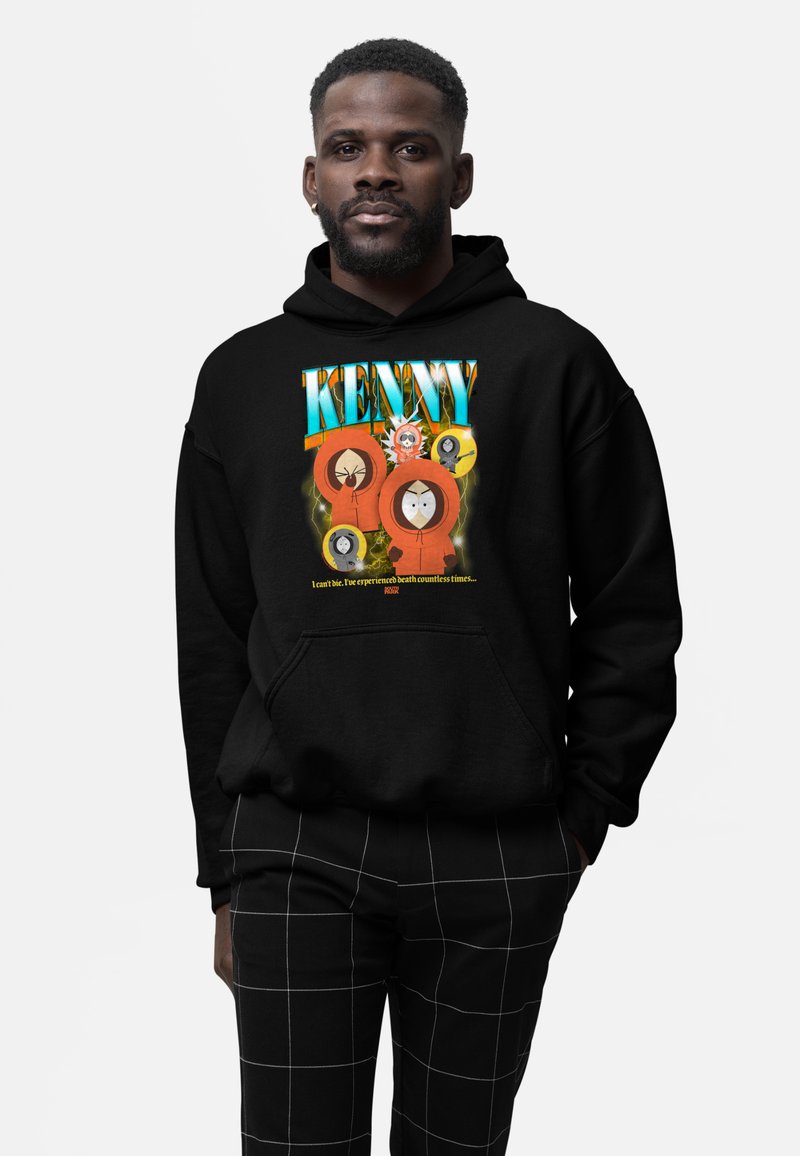 Homme portant un sweat à capuche noir avec des personnages de dessin animé colorés "Kenny" et un texte sur la mort à l'avant, associé à un pantalon noir à motif à carreaux.