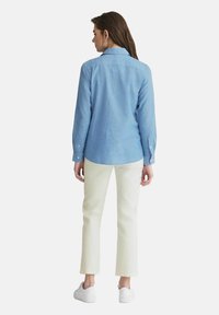 Lyseblå, langærmet skjorte med kravehals, skræddersyet pasform og knap-lukninger ved ærmerne, parret med cremfargede, cropped bukser og hvide sneakers.