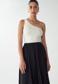 White ribbed one-shoulder top paired with a black pleated skirt. The top has a fitted silhouette; the skirt features an elastic waistband.