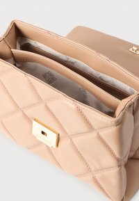 Μπεζ καπιτονέ δερμάτινο τσαντάκι χειρός με χρυσό κούμπωμα, που δείχνει πολλαπλές εσωτερικές θήκες με επένδυση από υφασμάτινη ετικέτα.