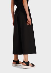 Pantaloni neri a gamba larga abbinati a sandali neri con suola bianca spessa, cinturino regolabile e accenti metallici. Design liscio e moderno.