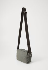 Zelená plátená crossbody taška s obdlžníkovým tvarom, kontrastným hnedým popruhom, striebornými detailmi a hlavným oddelením na zips. Textúrovaný povrch.