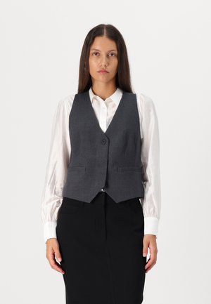 Gilet grigio realizzato in tessuto texturizzato con scollatura a V, chiusura a un bottone e due tasche frontali, indossato su una camicia bianca.