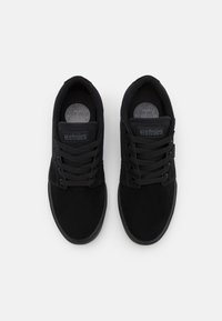 Black skate shoes with a suede and canvas upper, featuring round laces, a padded collar, and logo accents on the tongue.