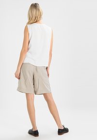 Top blanco sin mangas con un corte holgado, combinado con shorts beige hasta la rodilla. Los shorts tienen una textura suave y detalles plisados. Unos zapatos negros completan el atuendo.