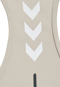 Top atletico beige con tessuto testurizzato, design a schiena scoperta e prominenti motivi a chevron bianchi con un accento verticale nero.