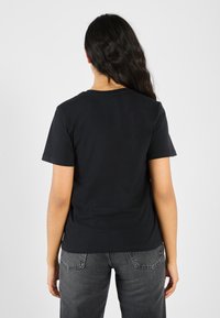 Svart bomull T-skjorte med korte ermer, rund hals og rett snitt. Kombinert med mørkegrå jeans, vist fra bak.