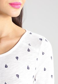 Weißes Kurzarmhemd mit kleinen marineblauen Segelboot-Mustern. Weicher, leichter Stoff mit Rundhalsausschnitt und subtilen Nähdetails.