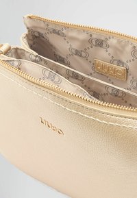 Pochette in pelle texturizzata oro con chiusura a zip, dotata di una fodera beige con motivo e di un piccolo etichetta logo all'interno. L'interno è diviso in due scomparti.