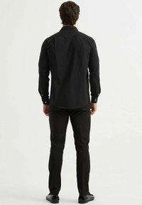 Chemise noire à manches longues avec une coupe droite, dotée d'un col boutonné, de poignets, et d'une texture lisse, assortie à un pantalon noir.