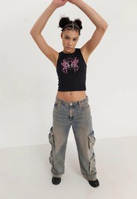 Top corto negro sin mangas con gráfico de mariposa rosa; pantalones cargo sueltos de color azul claro con grandes bolsillos; tela suave, corte relajado.