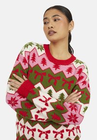 Maglione lavorato a maglia con un motivo festivo nei colori rosso, verde, rosa e bianco. I disegni includono alberi, fiocchi e fiocchi di neve con polsini a coste.