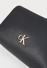 Črn usnjeni denarnica z teksturirano površino, s zlatim logotipom "CK". Kompaktna pravokotna oblika z zaobljenimi robovi.