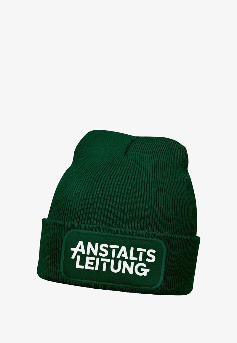 Green knit beanie with ribbed texture, featuring a fold-over cuff and a rectangular patch displaying the word "ANSTALTSLEITUNG" in white.
