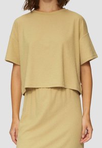 Beige geschnittenes T-Shirt aus strukturiertem Stoff. Kurze Ärmel, runder Ausschnitt und eine lockere Passform, die sich gut zum Schichten eignet.