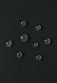 Klarer Wassertropfen in verschiedenen Größen auf einer strukturierten schwarzen Stoffoberfläche, die eine Kombination aus Glanz und Klarheit vor dem dunklen Hintergrund zeigen.