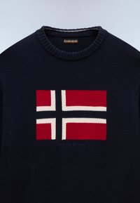 Jersey de punto azul oscuro con un diseño de cruz de estilo noruego en rojo, blanco y negro en el pecho y cuello redondo.