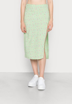 Saia floral verde menta com uma fenda lateral, feita de tecido suave, com pequenas flores rosas e amarelas, combinada com ténis brancos.