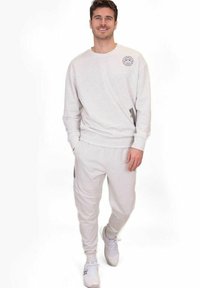 Hellgrauer Baumwollpullover mit Rundhalsausschnitt und kleinem Logo auf der Brust, kombiniert mit passenden Sweatpants mit Seitentaschen und schmal zulaufenden Knöcheln.