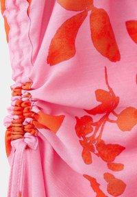Tissu rose avec couture froncée et détail d'impression florale orange vif sur tissu texturé.