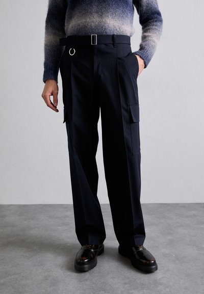 Pantalon cargo bleu marine avec une coupe décontractée, deux poches latérales, et une ceinture avec une boucle en métal. Associé à des chaussures noires vernis.