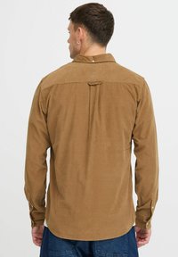 Brown corduroy shirt with long sleeves, subtle texture, classic collar, single back pleat, and buttoned cuffs, designed for a relaxed fit.
