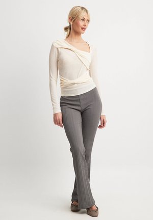 Cream long-sleeve top with draped neckline; smooth texture. Gray ribbed flared pants; fitted silhouette with subtle vertical lines. Brown ballet flats.