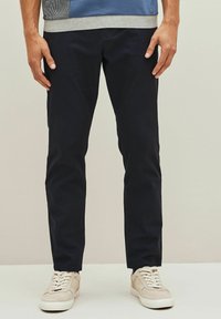 Tumedate sinised slim-fit chinos, mis on valmistatud puuvillast ja millel on sile tekstuur. Omab külgtaskuid ja on koos beežide vabaaja sneakersitega.