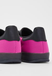 Adidas cipők textúrált rózsaszín anyag felsőrésszel, fekete sarokkal és gumitalppal. Az hátul található logó dombornyomása és a kényelemre tervezett kialakítás jellemzi őket.