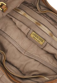 Interno di una borsa in pelle marrone con fodera in tessuto beige, dotato di una tasca con zip dorata e un'etichetta con la dicitura "CATERINA LUCCHI, MADE IN ITALY."