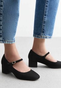 Scarpe Mary Jane nere in suede con punta rotonda, tacco basso a blocco e una sottile fascia con fibbia circolare in oro.