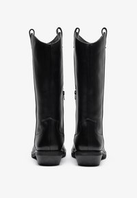 Botas de montar de cuero negro con un diseño alto, puntas afiladas y cremalleras laterales. Cuentan con suelas resistentes y detalles de costura visibles.